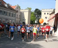 Een groep hardlopers in sportkleding loopt door een straat in de stad, waarbij sommigen een oranje ballon vasthouden.