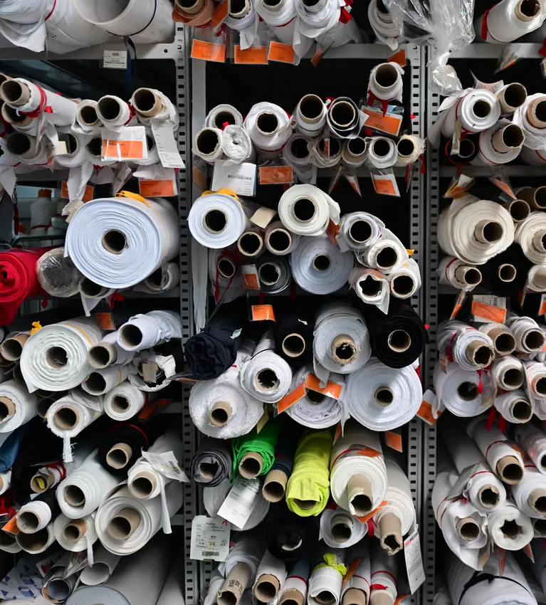 Planken vol met verschillende stofrollen in verschillende kleuren en maten, opgeslagen voor de productie van aangepaste sportkleding.