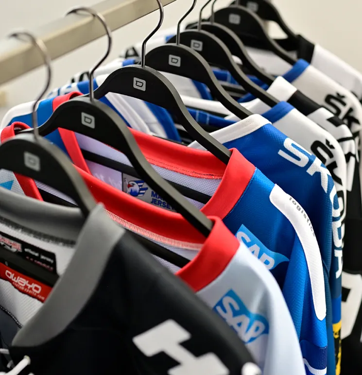 Een rij gekleurde, op maat gemaakte sportkleding van owayo hangt aan zwarte kledinghangers aan een kledingrek.