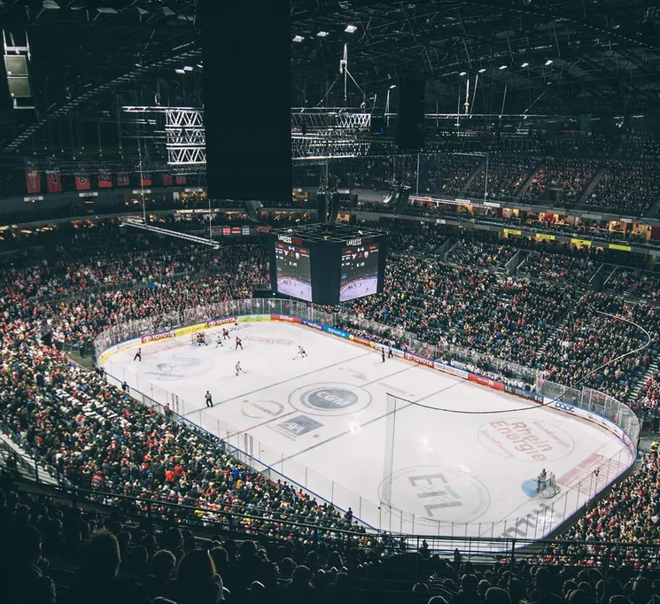 Een brede kijk op een vol ijshockeystadion met spelers op het ijs en een groot scorebord.