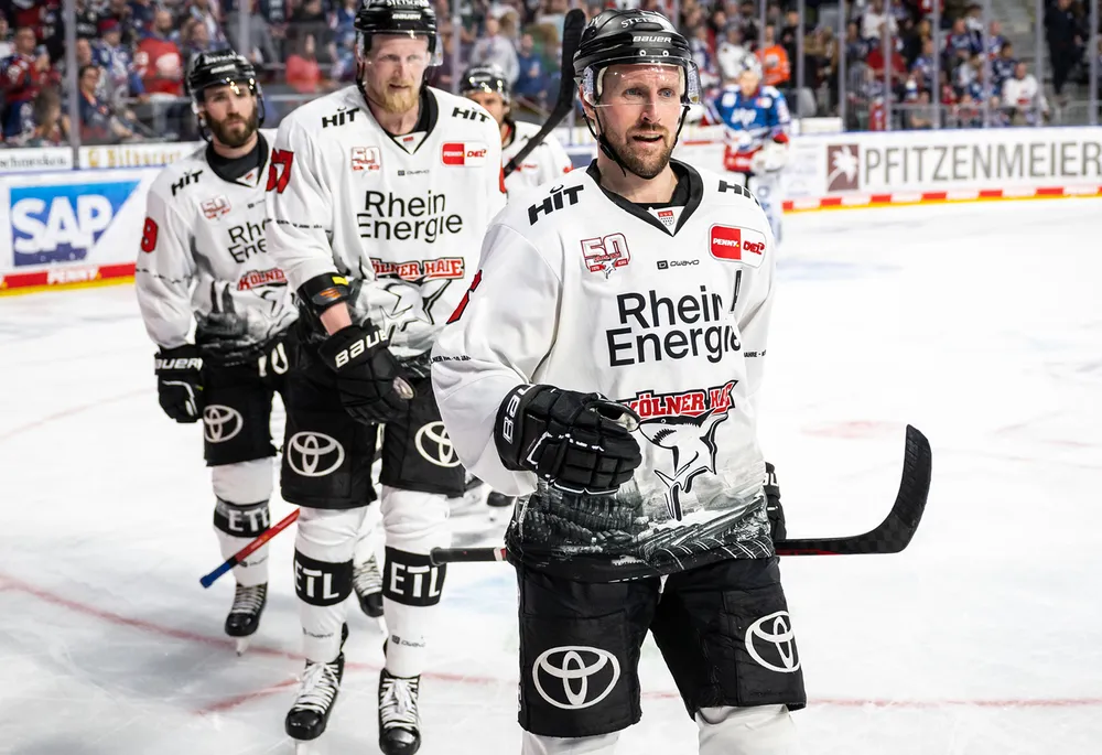 IJshockeyspelers in witte shirts met zwarte broeken met een teamlogo, staande op het ijs.