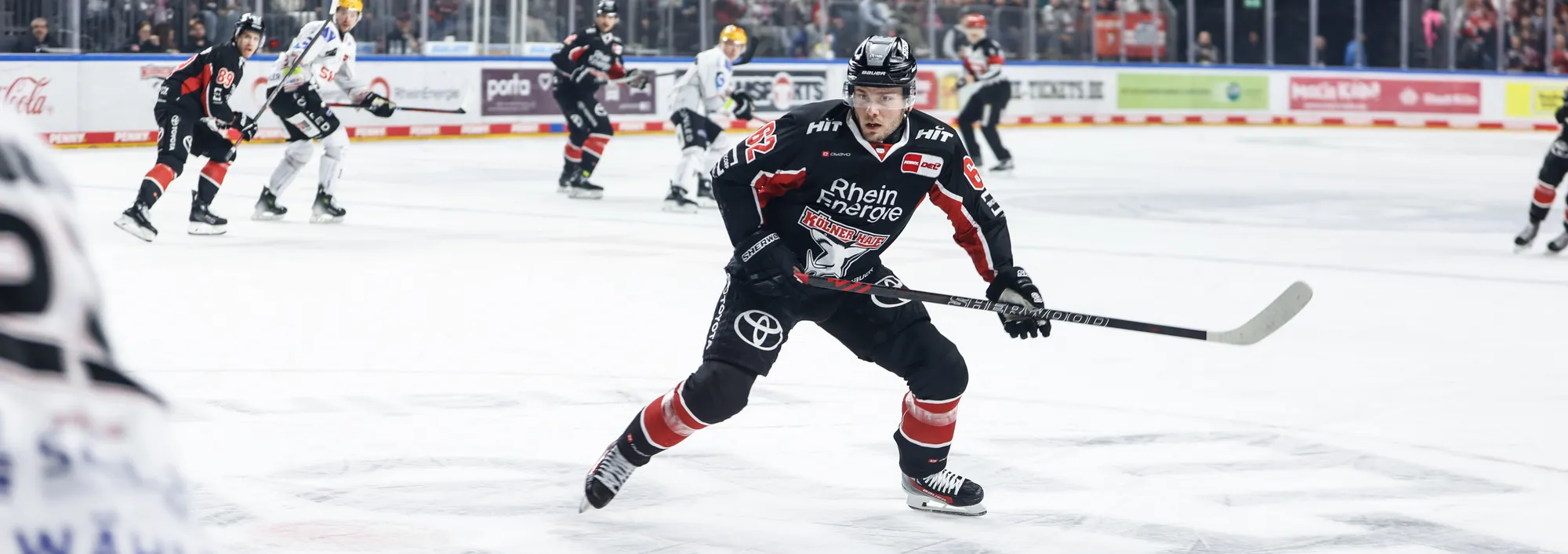 Een ijshockeyspeler in een zwart en rood shirt die op het ijs schaatst met een hockeystick.
