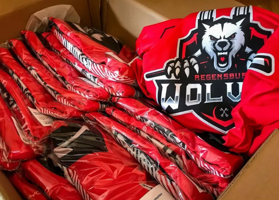 Een doos gevuld met rode, aangepaste sportkleding, waaronder een shirt met een wolflogo en de tekst 'Regensburg Wolves'.