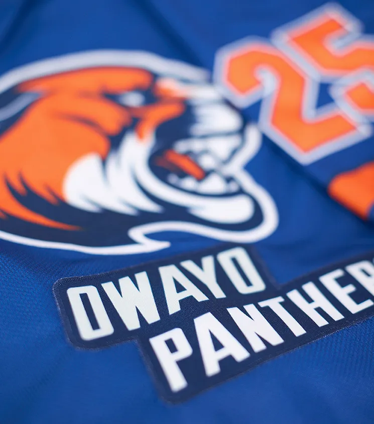 Nabijgezien van een blauw sportshirt met een oranje panterlogo en de tekst 'OWAYO PANTHERS' in witte letters op een donkere patch.
