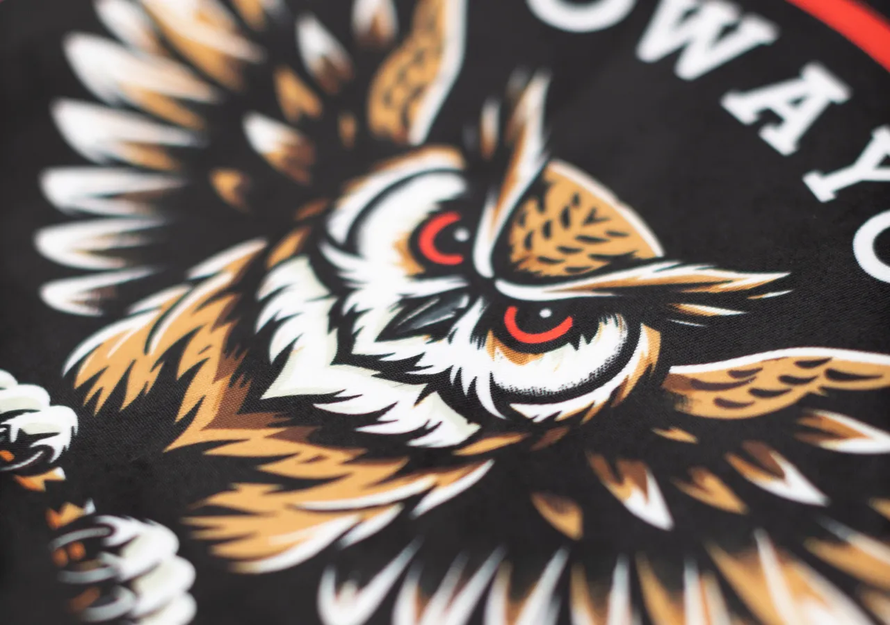Close-up van een gedetailleerd uilenontwerp op zwarte stof, dat kracht en dynamiek symboliseert.