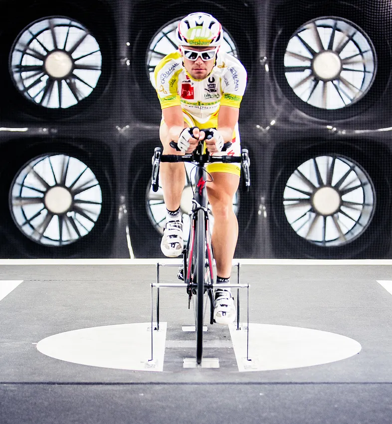 Een fietser in een aerodynamische houding op een fiets in een windtunnel, om de prestaties van aangepaste sportkleding te testen.