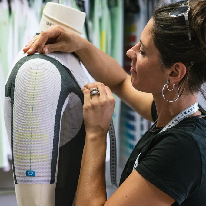 Een vrouw past een op maat gemaakt sportkledingstuk aan op een mannequin terwijl ze een meetlint draagt.