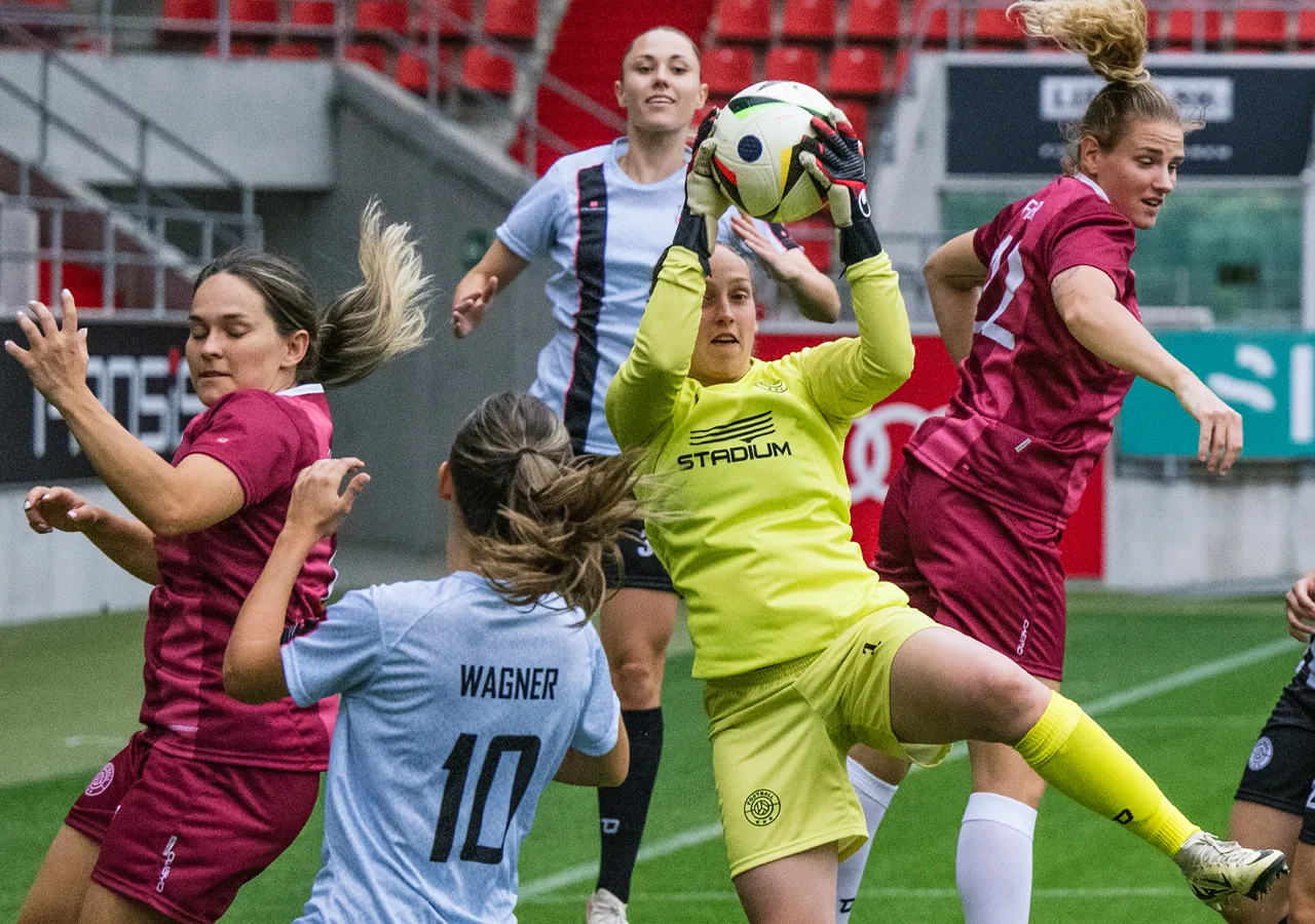 Een doelverdediger in gele sportkleding vangt een voetbal terwijl andere speelsters in verschillende shirts strijden om de bal.