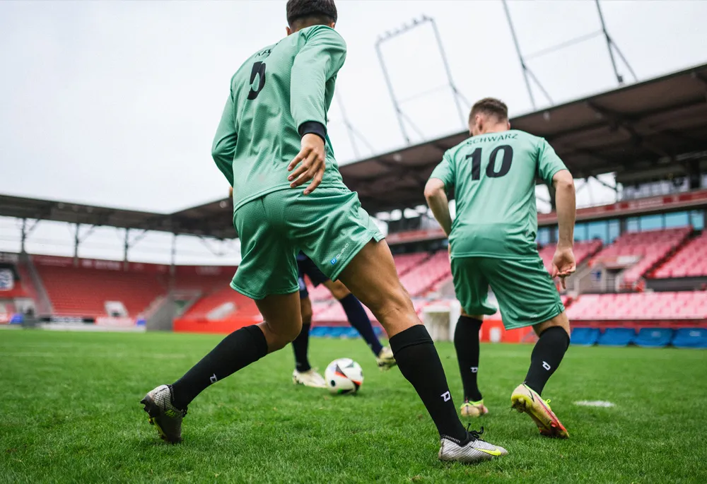 Twee voetballers in groene shirts en zwarte sokken die op een grasveld spelen.