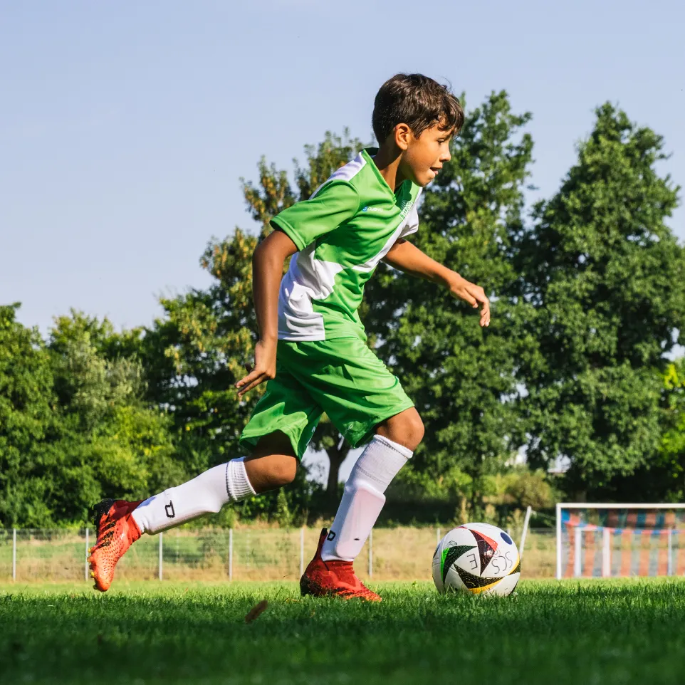 Een jonge voetballer in groene en witte sportkleding rent over een voetbalveld.