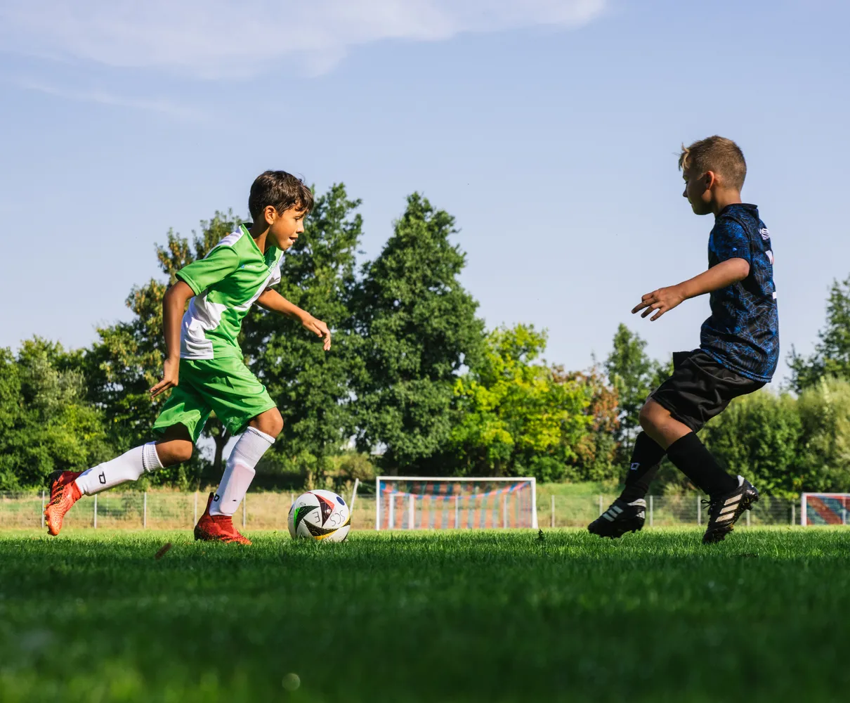 Een jonge voetballer in een groen shirt rent met de bal op een grasveld.