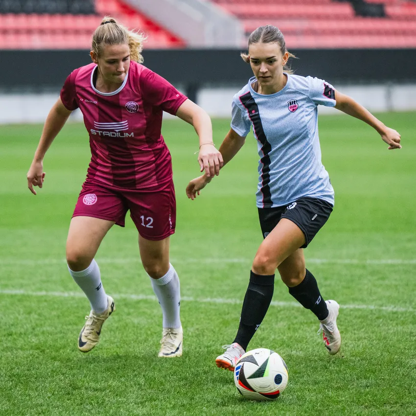 Twee vrouwen in sportkleding spelen voetbal op een groen veld.