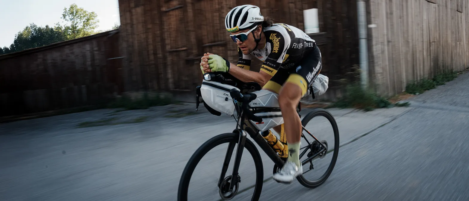 Een fietser in een aerodynamische houding op een wegfiets, die aangepaste sportkleding van owayo draagt, terwijl hij op een straat rijdt.