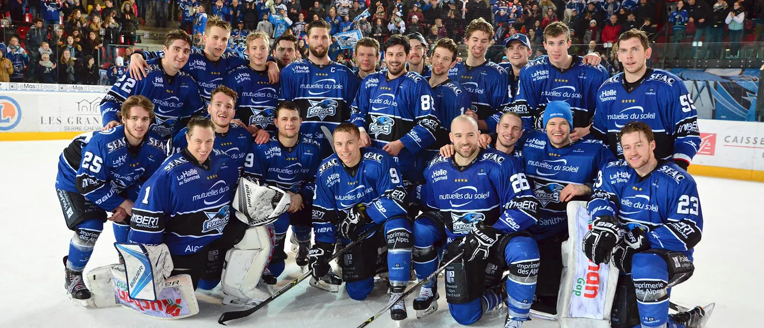 Een ijshockeyploeg in blauwe shirts met het logo van de Rapaces de Gap poseert op het ijs voor een publiek.