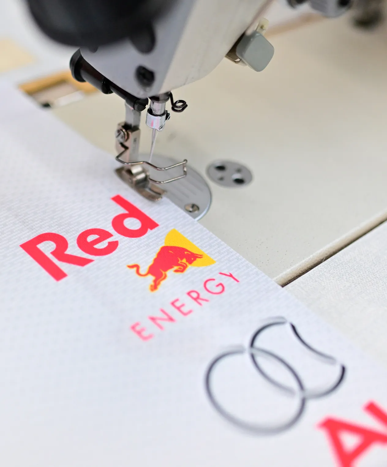 Een naaimachine naait een wit sportkledingstuk met het Red Bull Energy-logo.