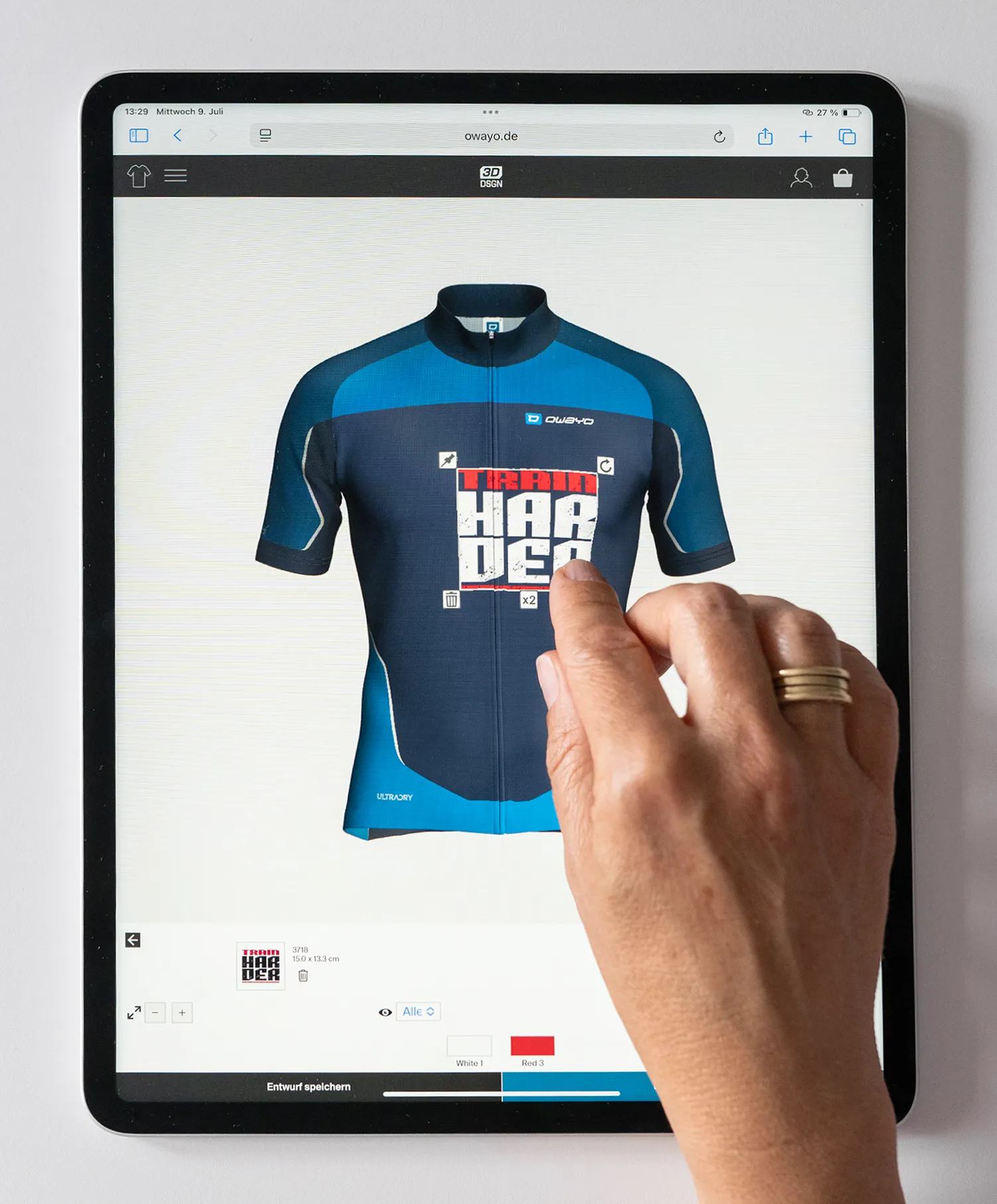 Een hand bedient een tablet met de owayo-website, waarop een aangepast blauw en donkerblauw fietsshirt met de tekst 'TRAIN HARDER' te zien is.