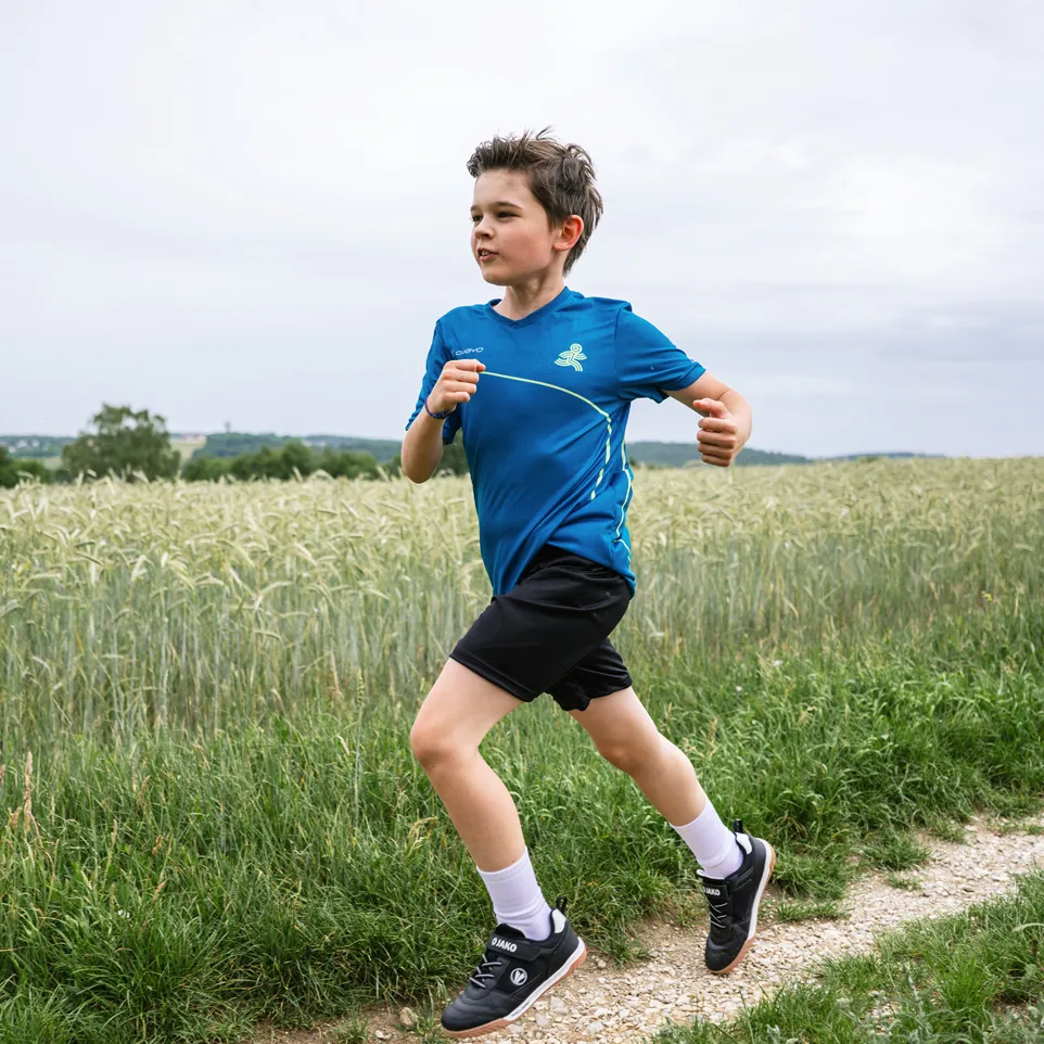 Een jongen rent op een zandpad, gekleed in een blauwe sportshirt en zwarte shorts.