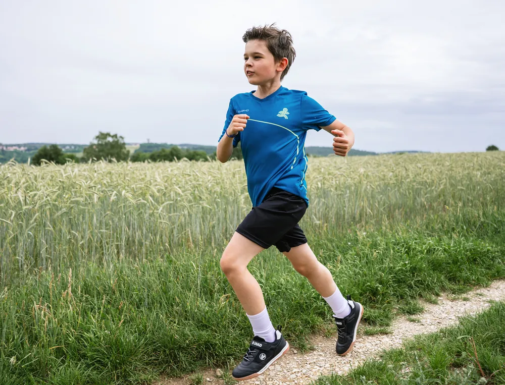 Een jongen rent op een zandpad, gekleed in een blauw sportshirt en zwarte shorts.