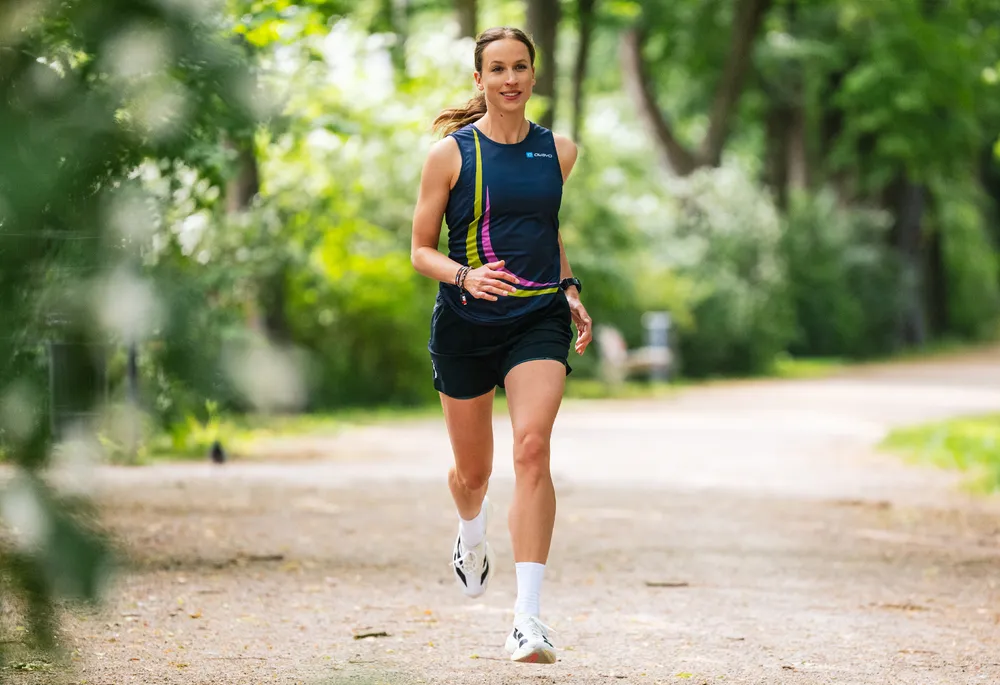 Een sportieve vrouw loopt op een pad buiten, gekleed in een blauwe sporttanktop met kleurrijke accenten en shorts.