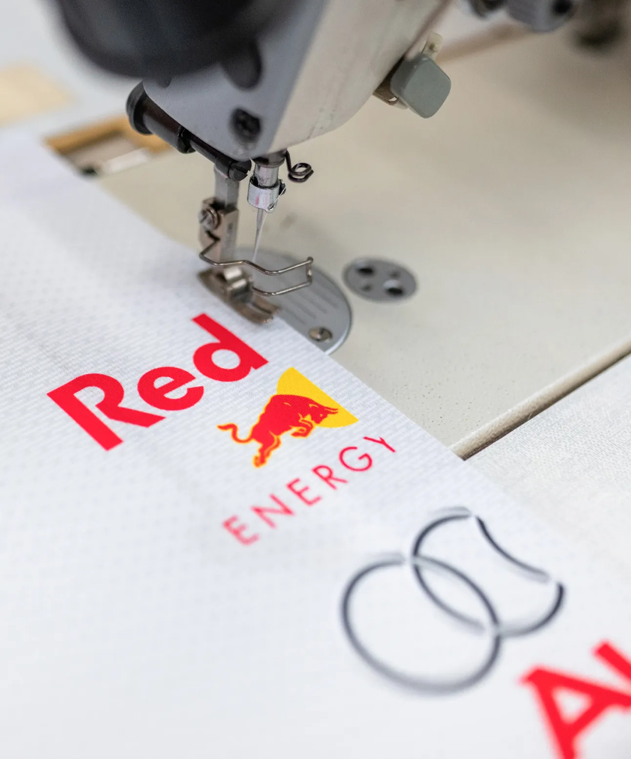 Een naaimachine bewerkt een stuk stof met bedrukte logo's en tekst.