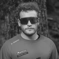 Een man met krullend haar en zonnebril draagt een grijze, lange mouwen sportshirt met het 'owayo' logo op de schouder en andere sponsorlogos op de borst.