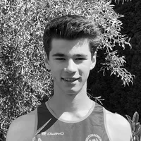 Een jonge man in een zwart en grijs mouwloos sportshirt met het 'owayo' logo op de borst, glimlachend voor een achtergrond van groene bladeren.