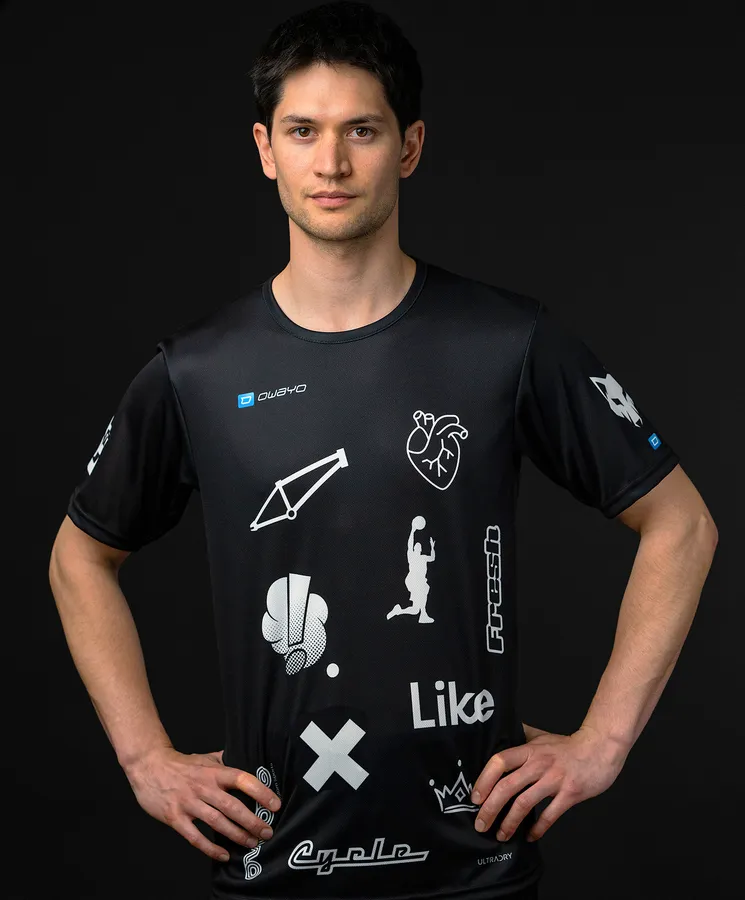 Een man draagt een zwart sportshirt met verschillende witte symbolen en logo's.