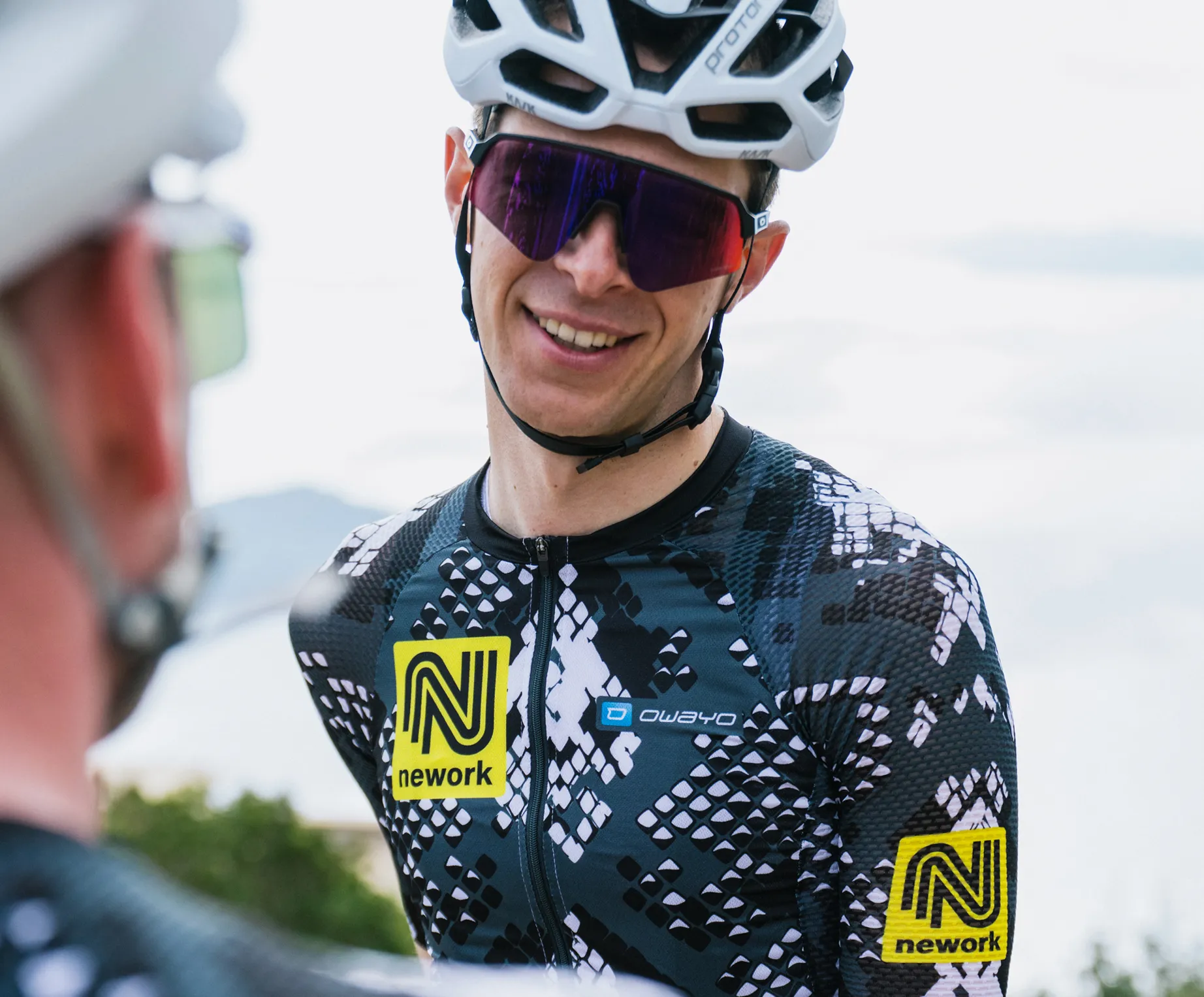 Een fietser draagt een op maat gemaakt zwart-wit geruit tricot met een geel 'nework'-logo en een 'owayo'-logo op de borst.