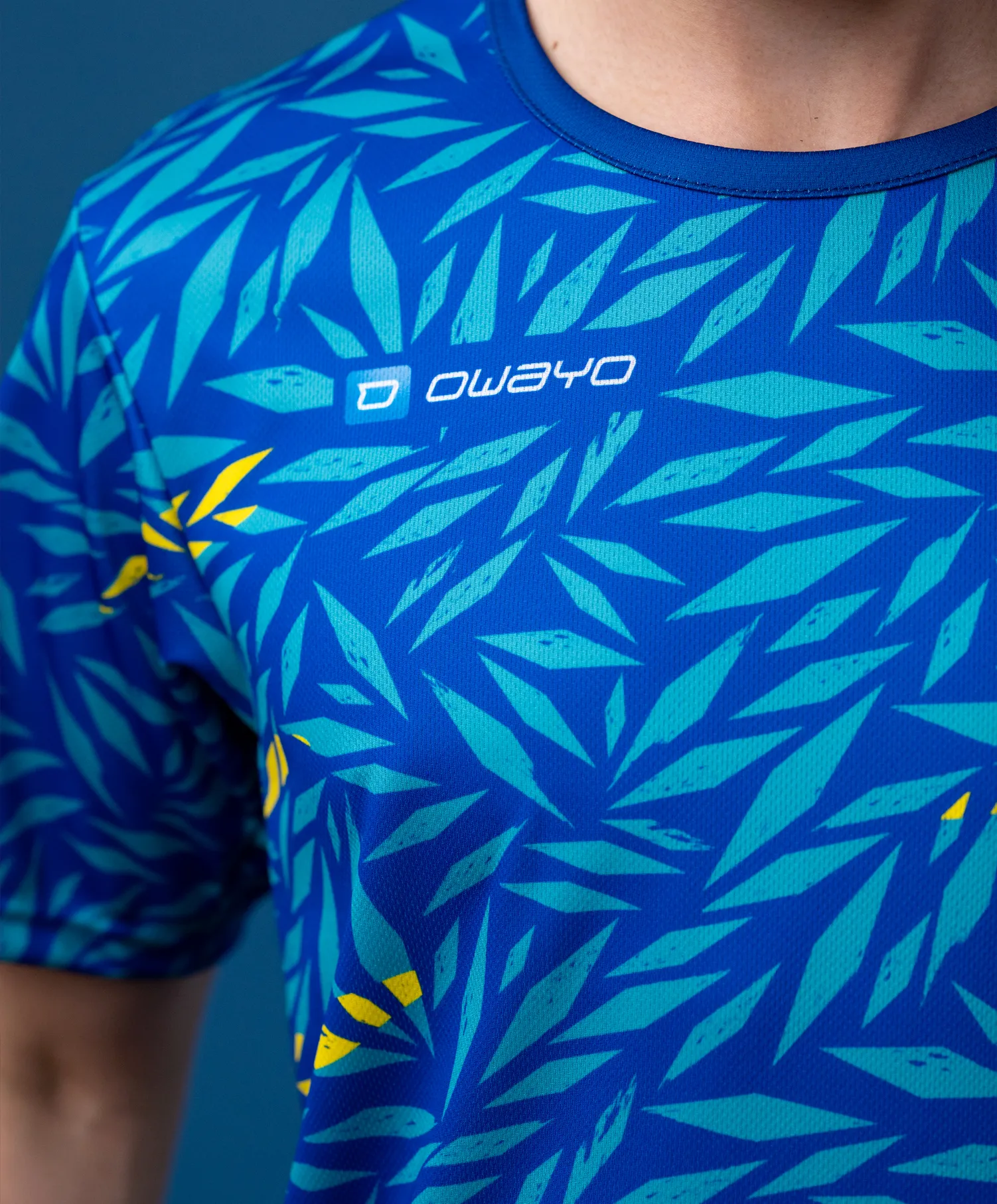 Een sportief, kort mouw shirt met een blauw bladvormig patroon in verschillende tinten groen met gele accenten.