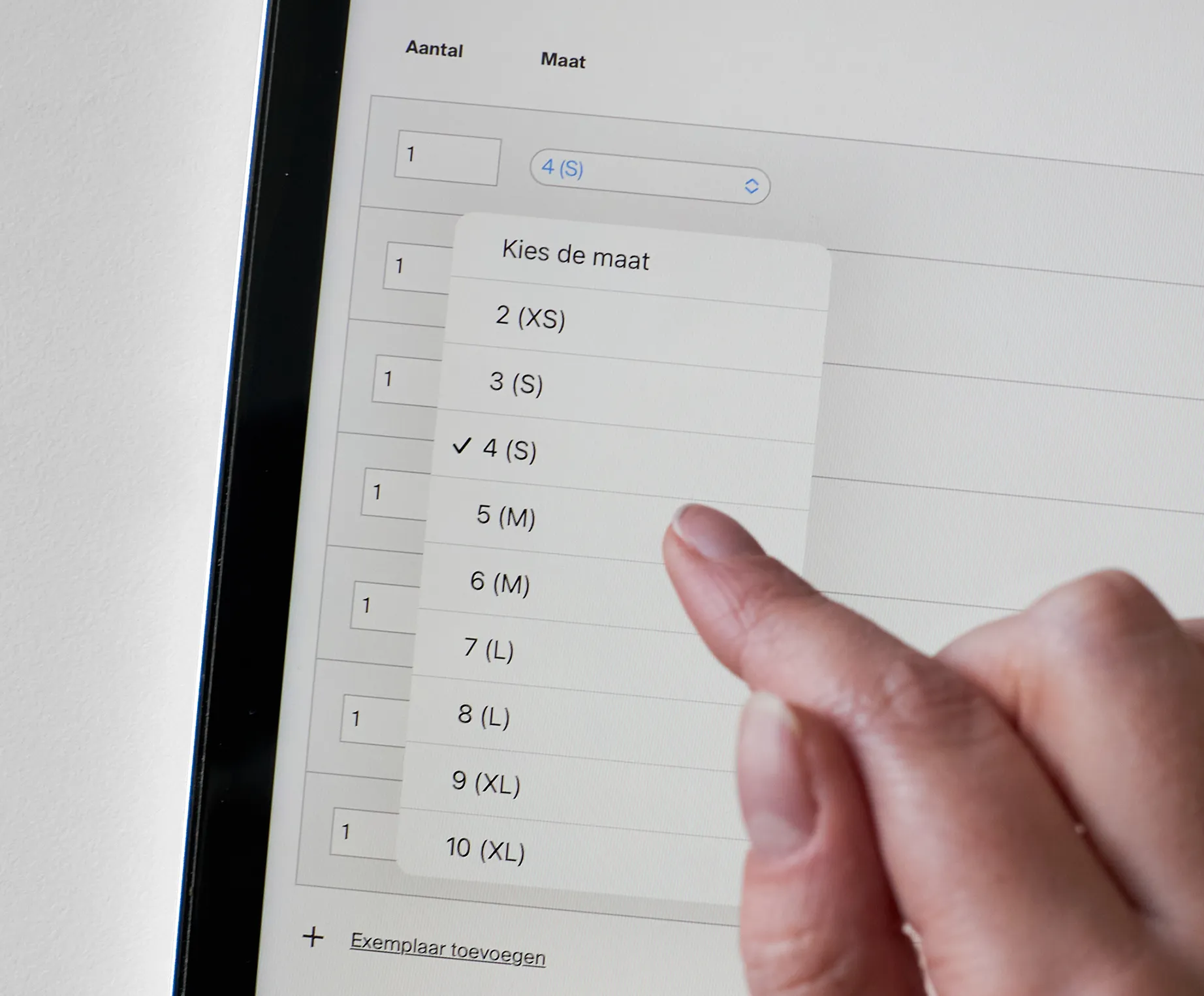 Een hand kiest maat 4 (S) uit een lijst op een tablet, terwijl op het scherm de opties voor aantal en maat van sportkleding worden weergegeven.