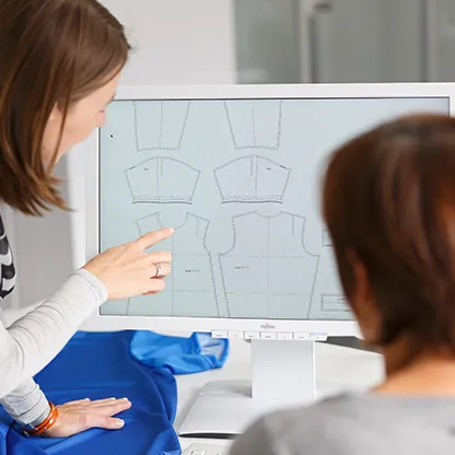 Twee personen bekijken digitale patronen voor sportkleding op een computerbeeldscherm, waarbij een persoon naar het scherm wijst.