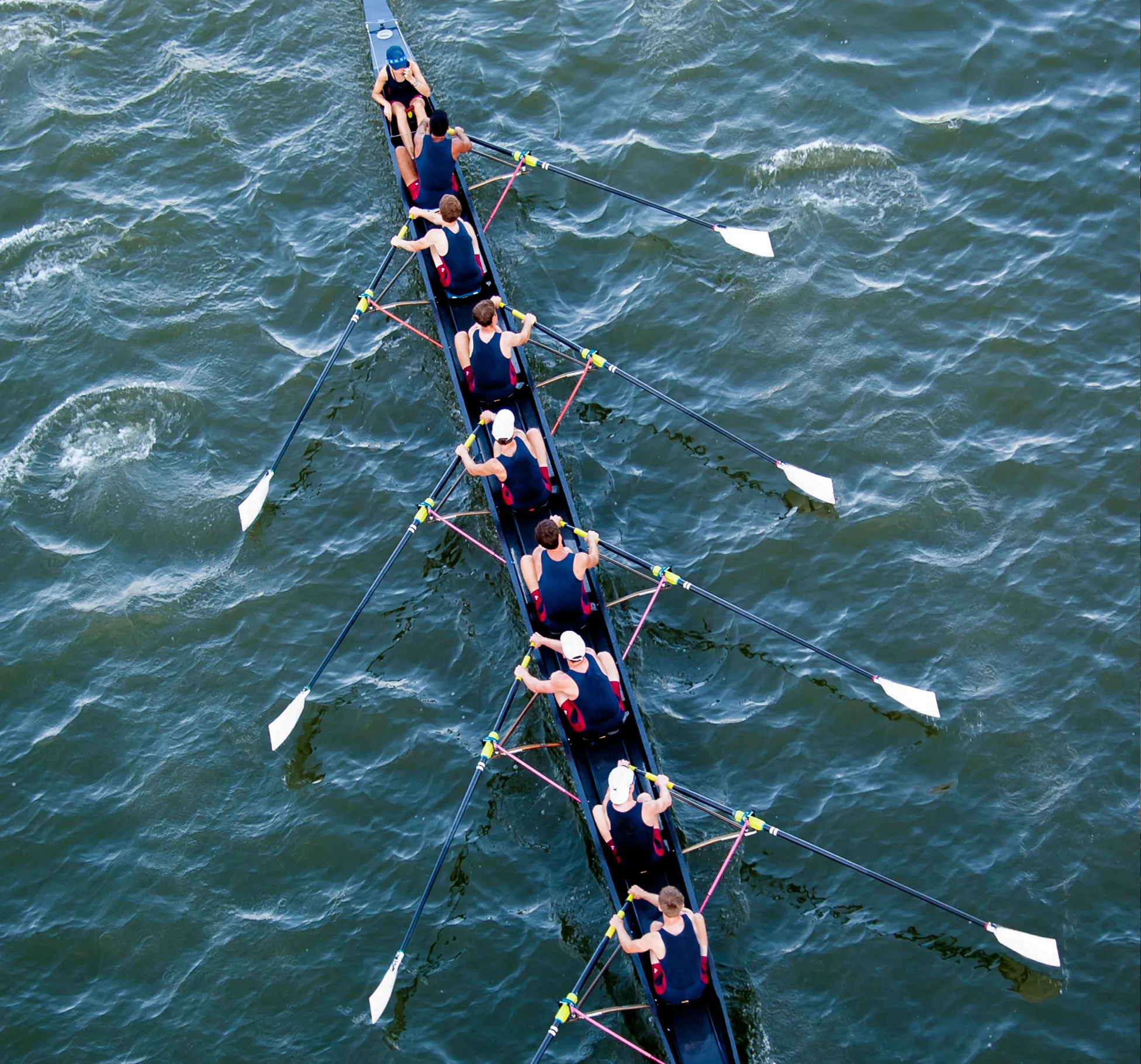 Een groep roeiers in bijpassende sportkleding roeit synchroon op een wateroppervlak.