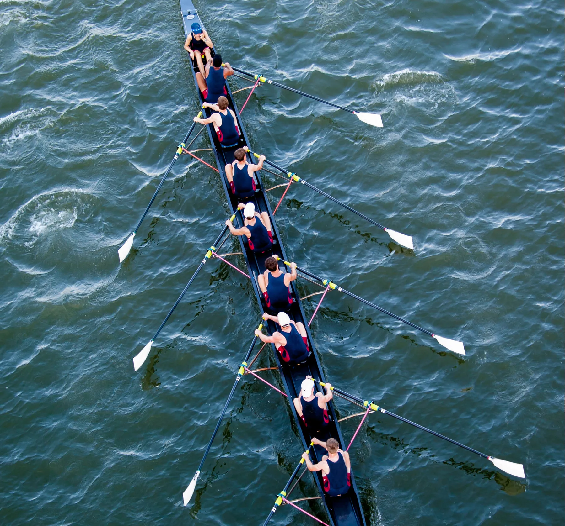 Een groep roeiers in bijpassende sportkleding roeit synchroon op een wateroppervlak.
