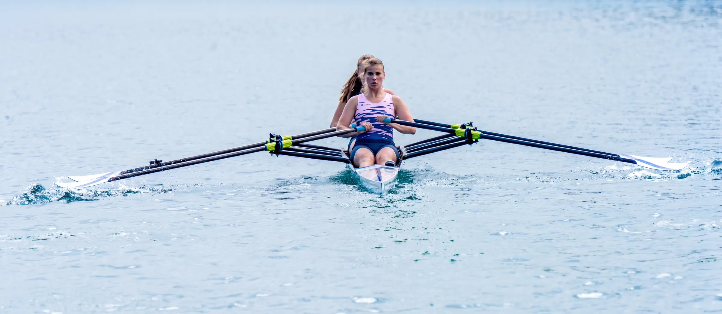 Een roeister peddelt in een eenpersoonsboot op kalm water.