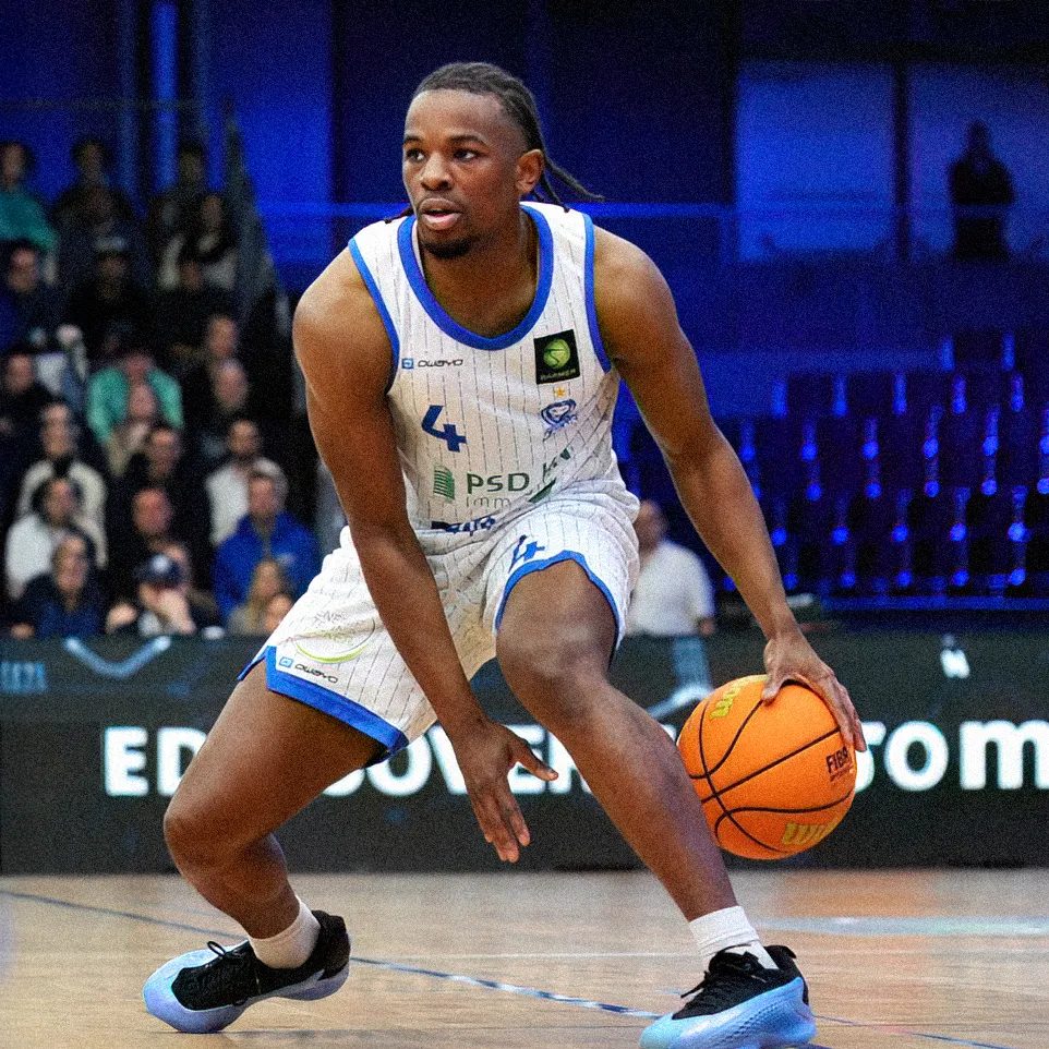 Een basketballer in een gestreept shirt dribbelt de bal op het veld.