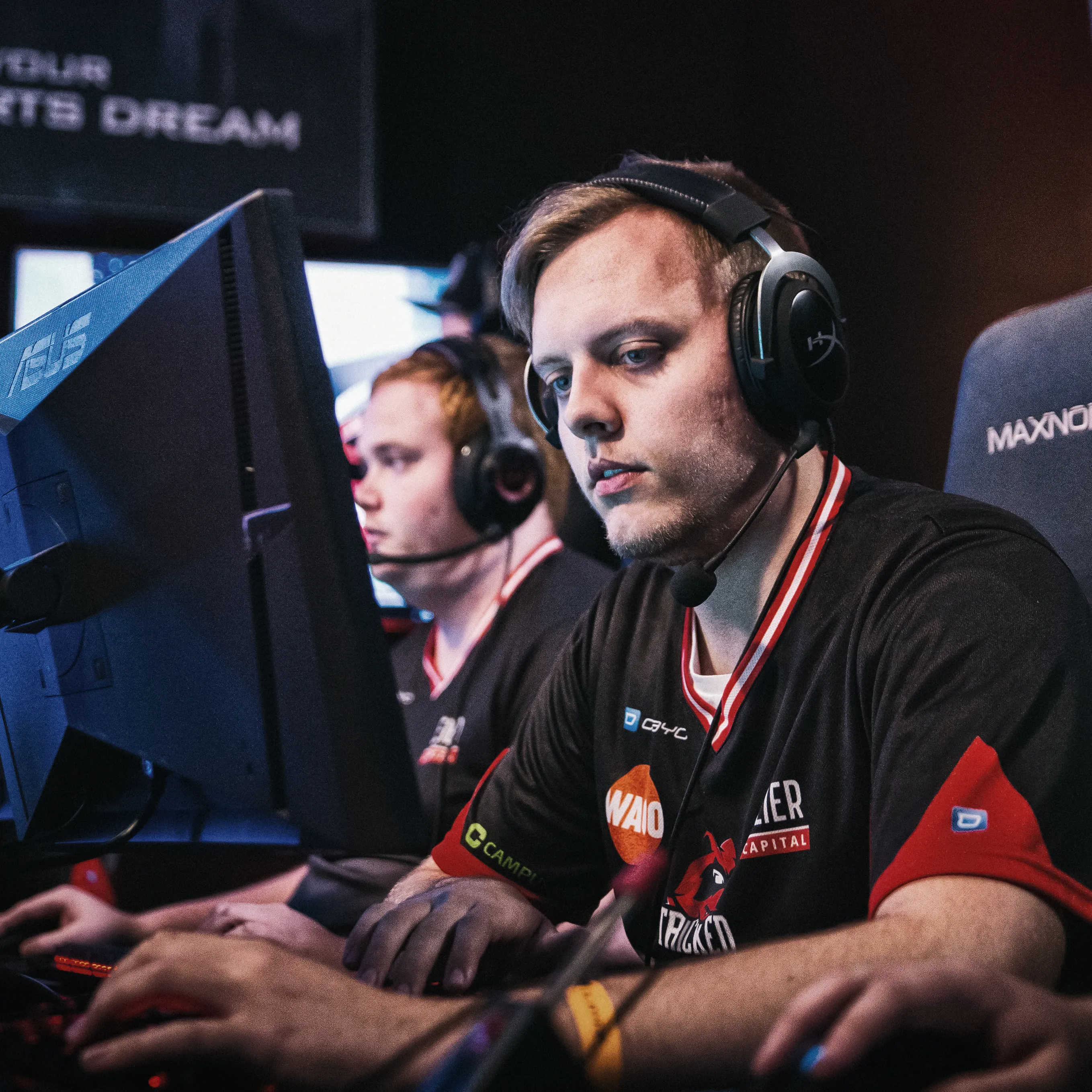Twee spelers in sportieve T-shirts met headsets, gefocust op hun computers tijdens een eSports-toernooi.