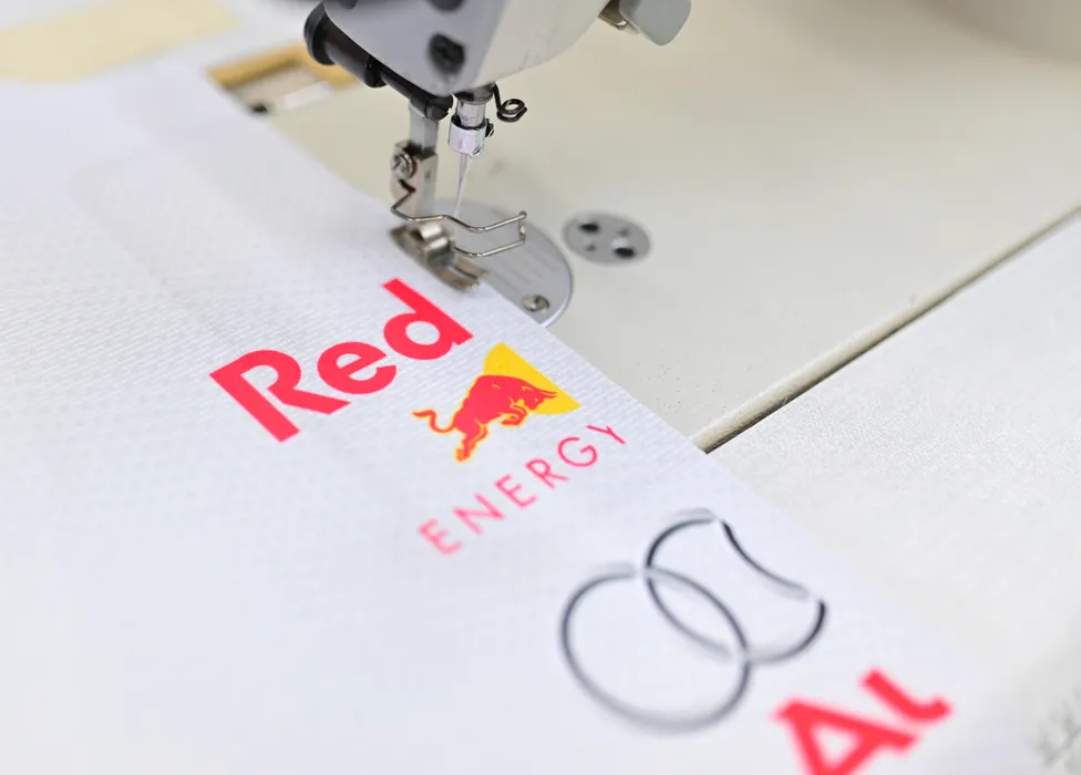 Een naaimachine naait een wit sportkledingstuk met het rode Red Bull Energy-logo en een ander logo.